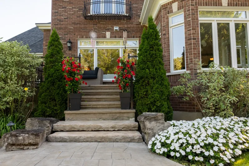 Stone steps rising to the house between cedars and red mandevilla planters