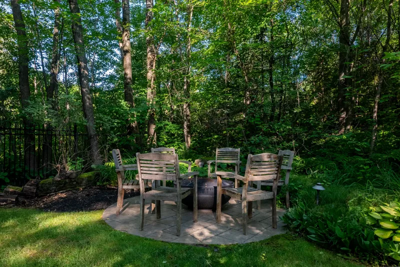 Wooden chairs around a fire bowl on a stone patio in the woodland garden