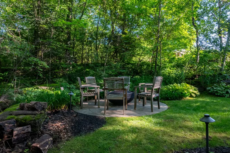 Wooden chairs around a fire bowl on a stone patio in the woodland garden