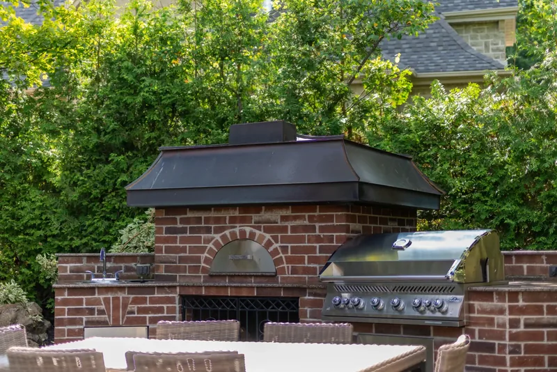 Brick outdoor kitchen with a wood-fired oven, a built-in grill, and a dining area