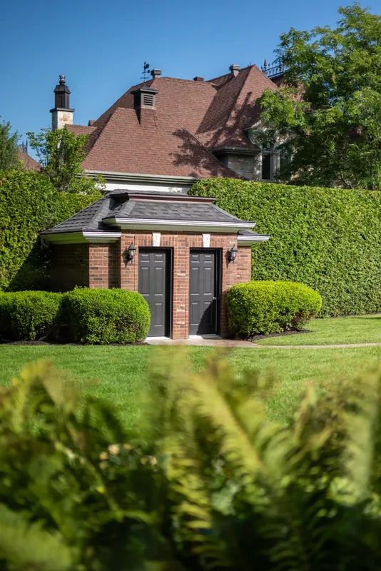 Brick garden pavilion framed by tall cedar hedges