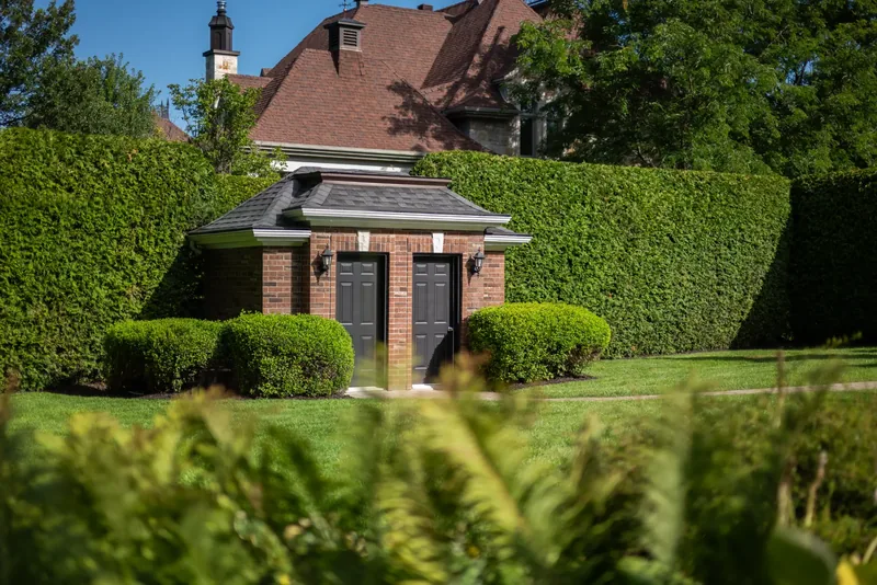 Brick garden pavilion framed by tall cedar hedges