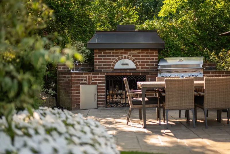 Brick outdoor kitchen with a wood-fired oven, a built-in grill, and a dining area