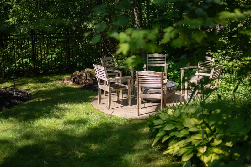 Wooden chairs around a fire bowl on a stone patio in the woodland garden