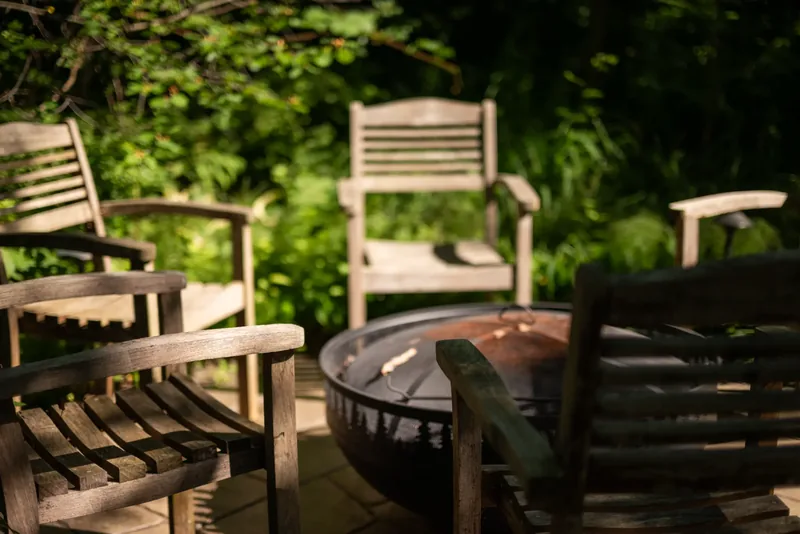Wooden chairs around a fire bowl on a stone patio in the woodland garden