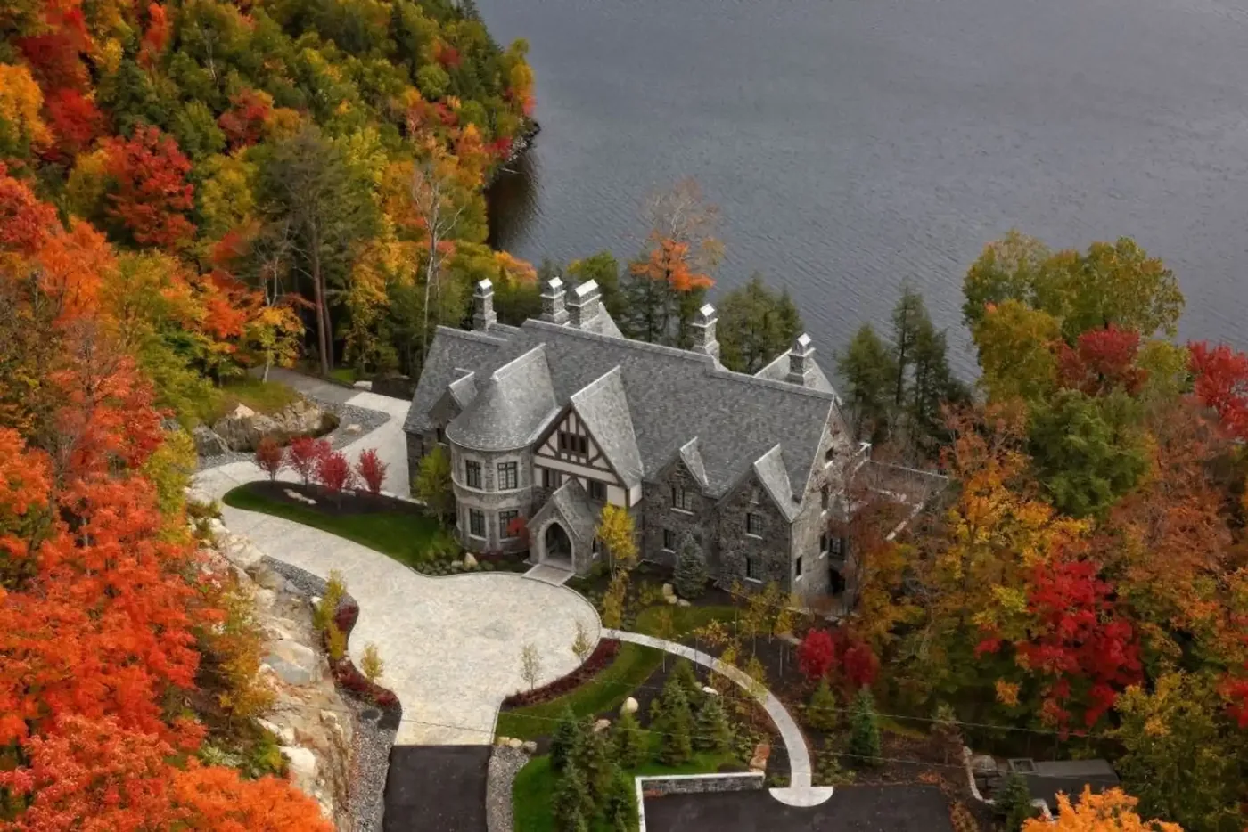 Aerial view of the stone estate and its curving drive among autumn colours on Lake Tremblant