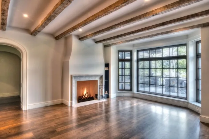 Living room with wood beams, a fireplace, and a curved wall of windows over the trees