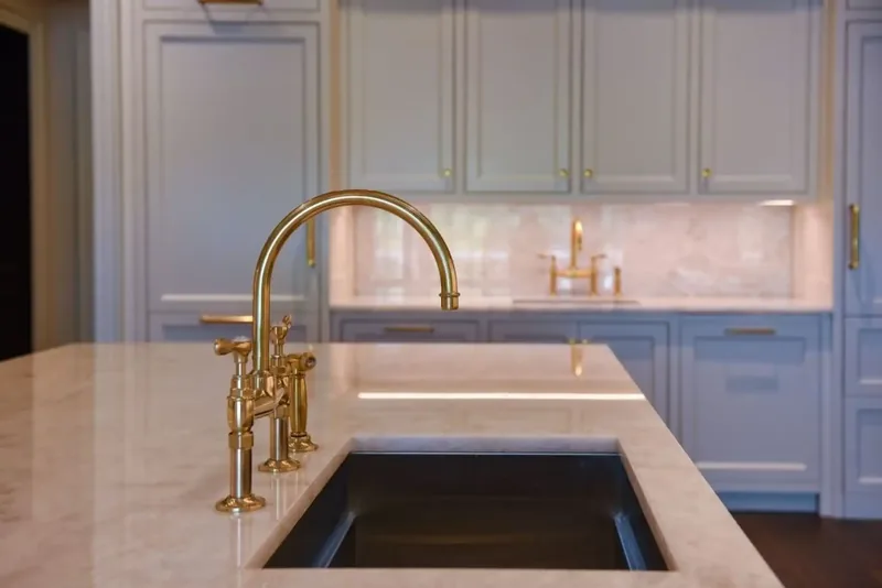 Kitchen island in white stone with a brass bridge faucet and custom cabinetry