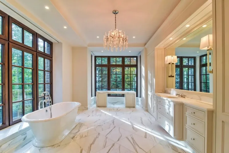 Bathroom with a freestanding tub, a marble floor, a crystal chandelier, and tall windows