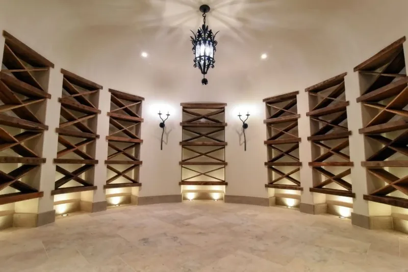 Wine cellar with lit wood racks, a stone floor, and a wrought-iron lantern