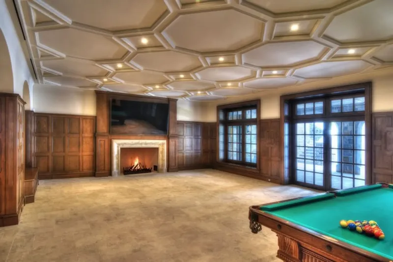 Games room fireplace beneath an octagonal coffered ceiling, with a billiard table in the foreground