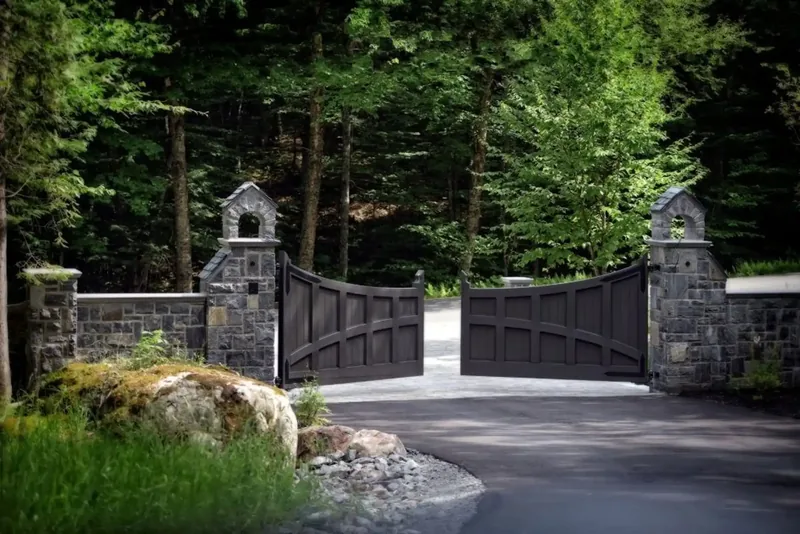 Stone gate piers and dark wood gates at the forested entrance drive