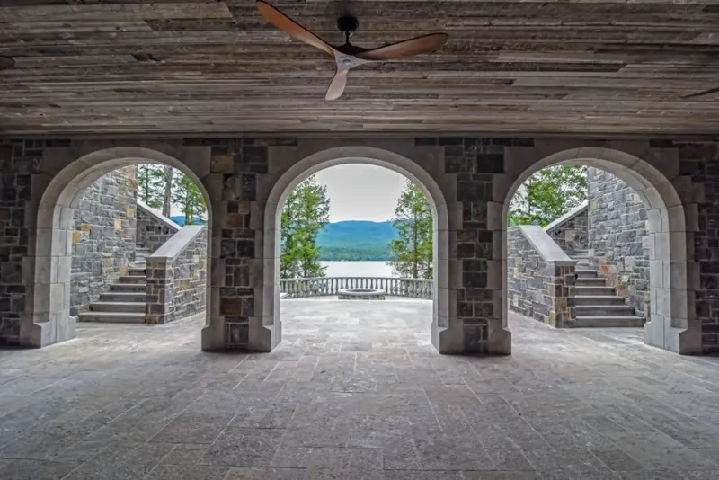 Stone arcade of three arches framing twin staircases and the lake, beneath a weathered wood ceiling
