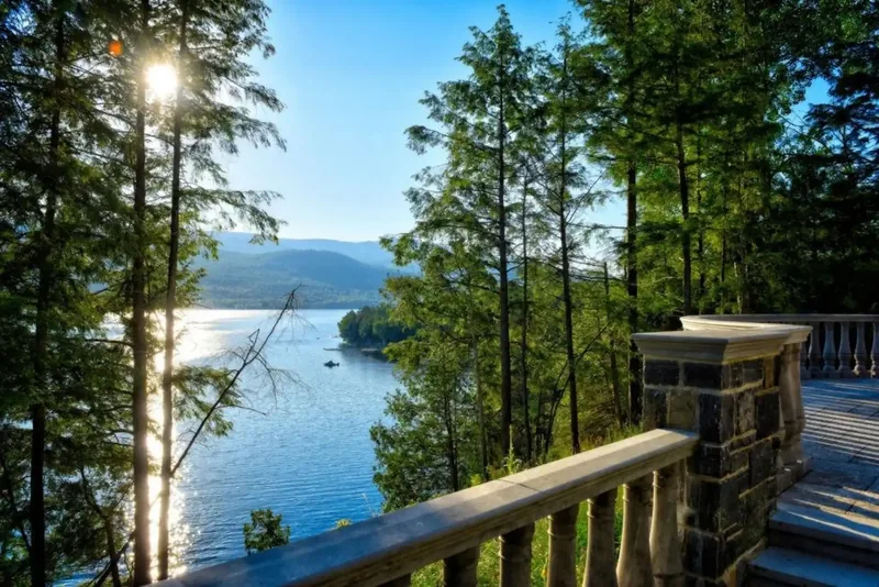 Stone terrace railing overlooking the sunlit lake through tall pines