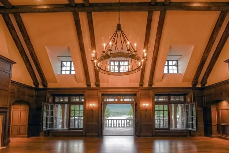 Great hall with exposed beams, dormer windows, and French doors opening to the lake terrace