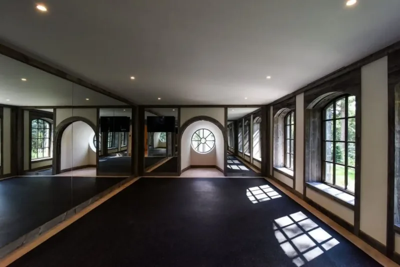 Long mirrored studio with a dark floor and arched windows along one side