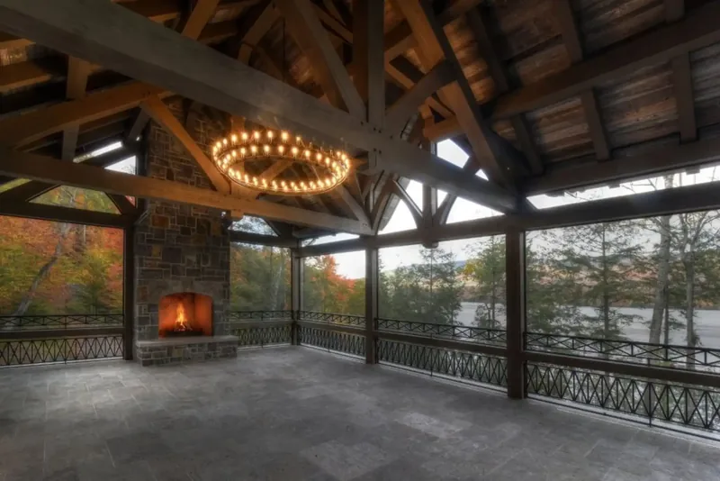 Timber-framed screened porch with a stone fireplace and a ring chandelier above the treetops