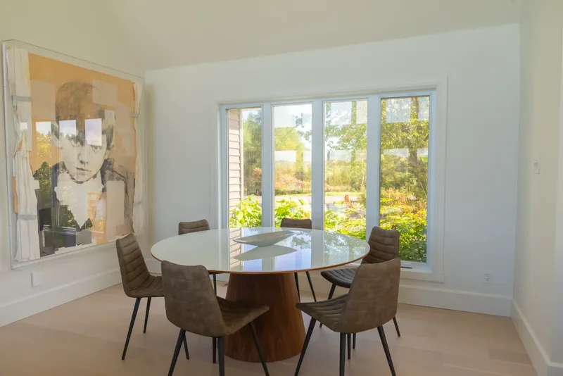 Round dining table on a wood pedestal beside garden doors and a large portrait artwork
