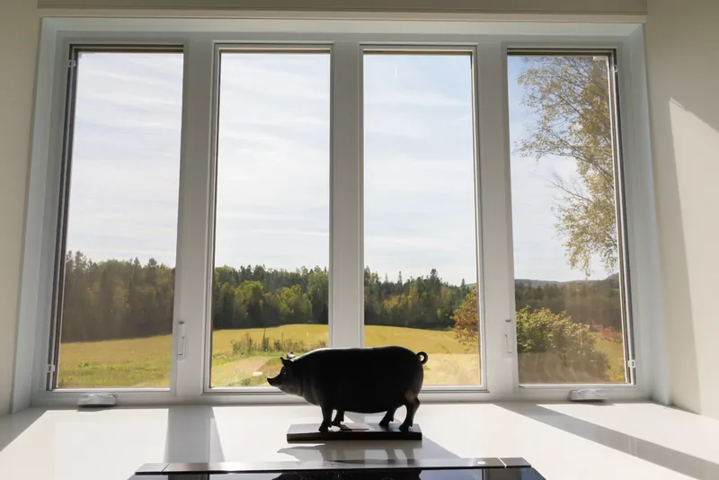 Black sculpture before tall windows overlooking fields and forest