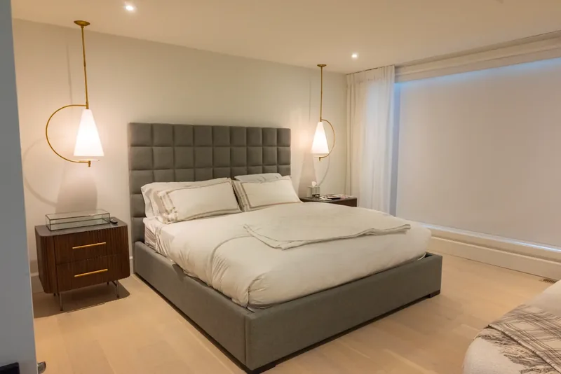Bedroom with a grey tufted headboard, brass pendant lights, and walnut nightstands