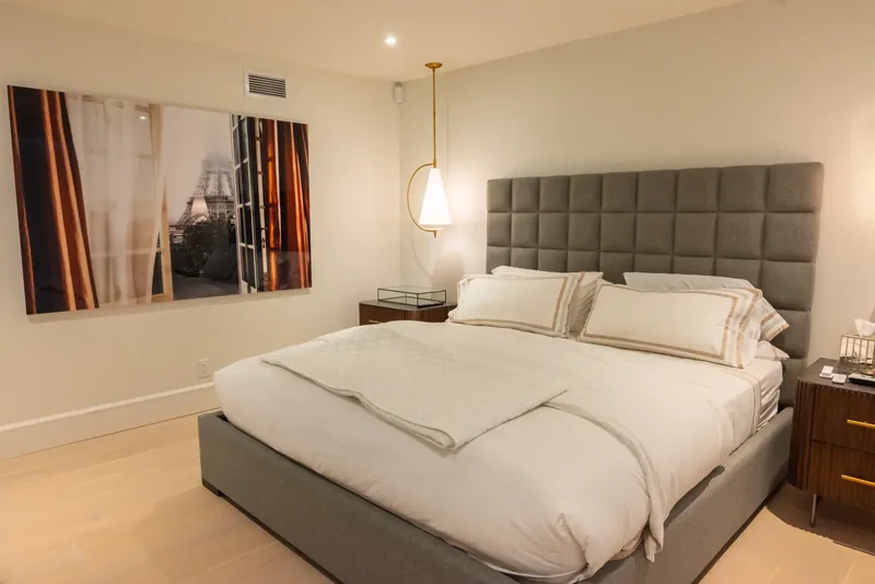 Bedroom with a grey tufted headboard, brass pendant lights, and walnut nightstands
