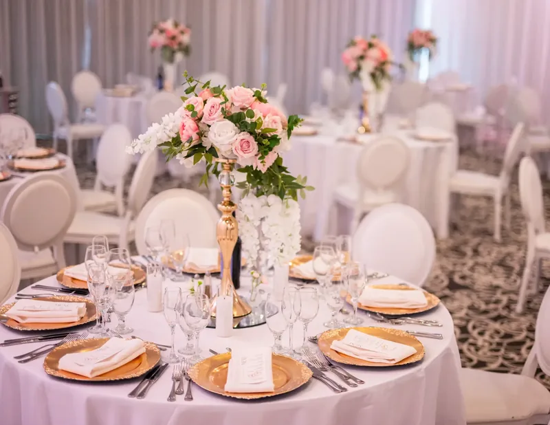 Round table with gold-rimmed chargers, folded napkins, and a blush and white rose centrepiece