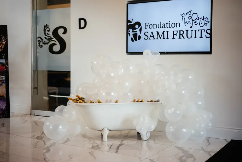 Clawfoot tub of champagne bottles and white balloons beside a frosted glass door with the S monogram