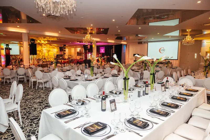 Hall set for a gala with long and round tables, calla lily centrepieces, chandeliers, and a lit stage at the back