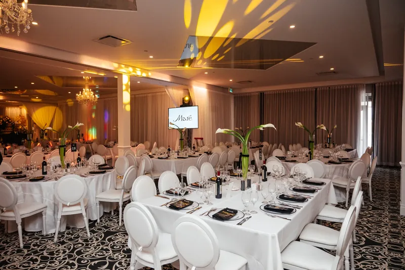 Banquet room with white tables and medallion chairs, calla lily centrepieces, and patterned light across the ceiling