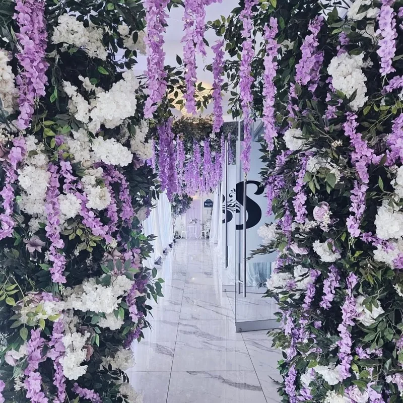 Wisteria and hydrangea arch framing a marble-look corridor and glass doors with the S monogram