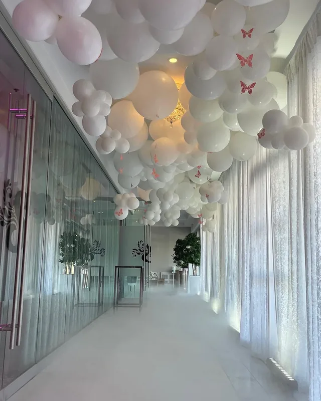 Corridor beside glass doors bearing the S monogram, with sheer drapes and a ceiling of white balloons