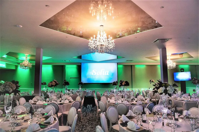 Main reception hall with crystal chandeliers in mirrored ceiling trays, green uplighting, and a screen showing the Sofia Reception Hall name