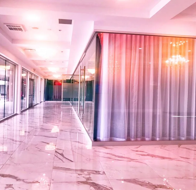 Lobby with polished veined tile, glass storefront windows, a coffered ceiling, and a glass-walled hall with sheer drapes